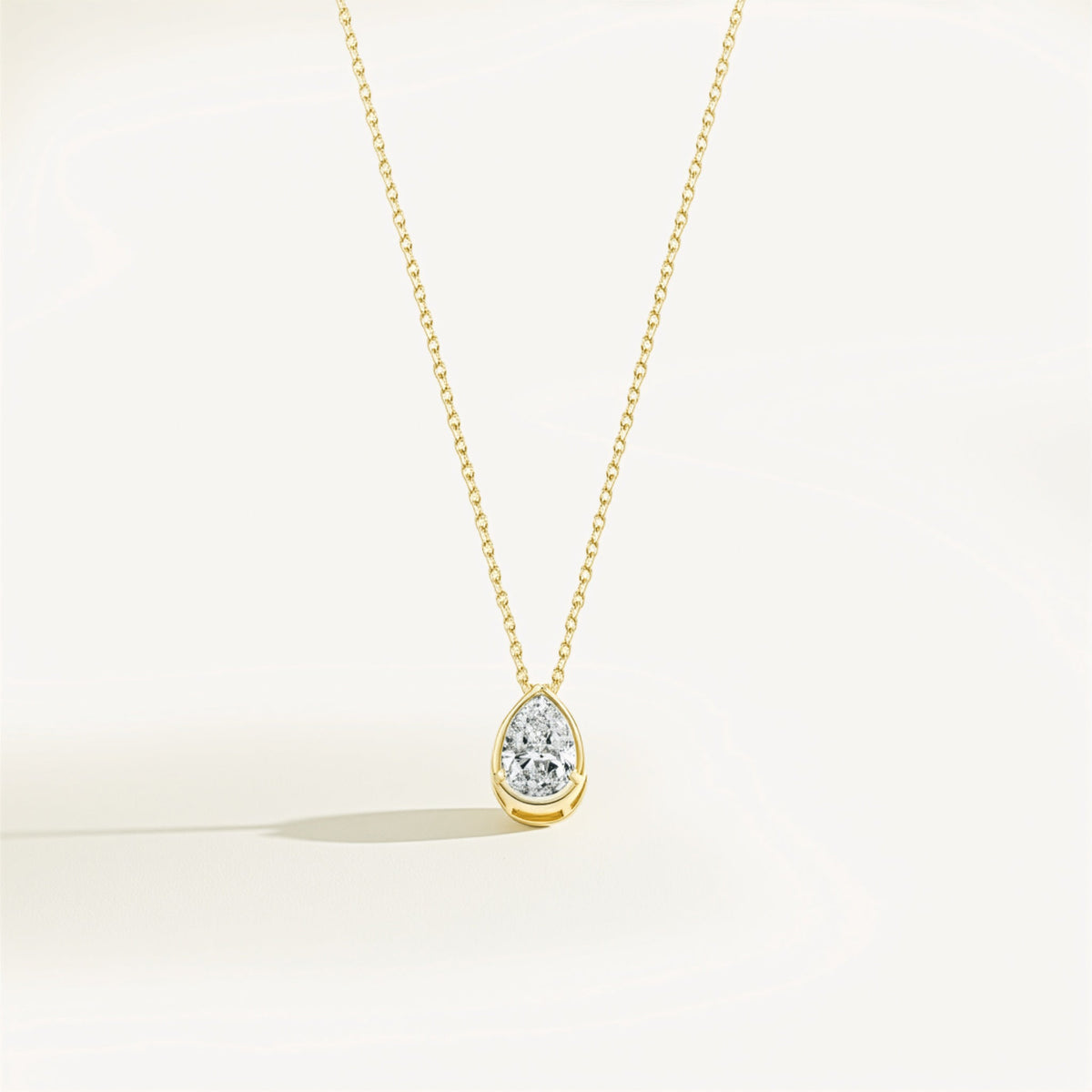 Gold necklace with a teardrop-shaped moissanite pendant on a light beige background