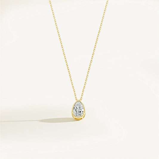 Gold necklace with a teardrop-shaped moissanite pendant on a light beige background